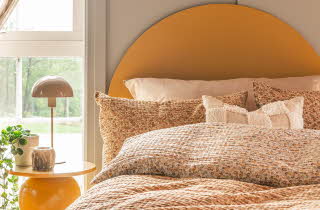 En gul seng redd opp med mange puter og en dyne, med et gult nattbord ved siden av
