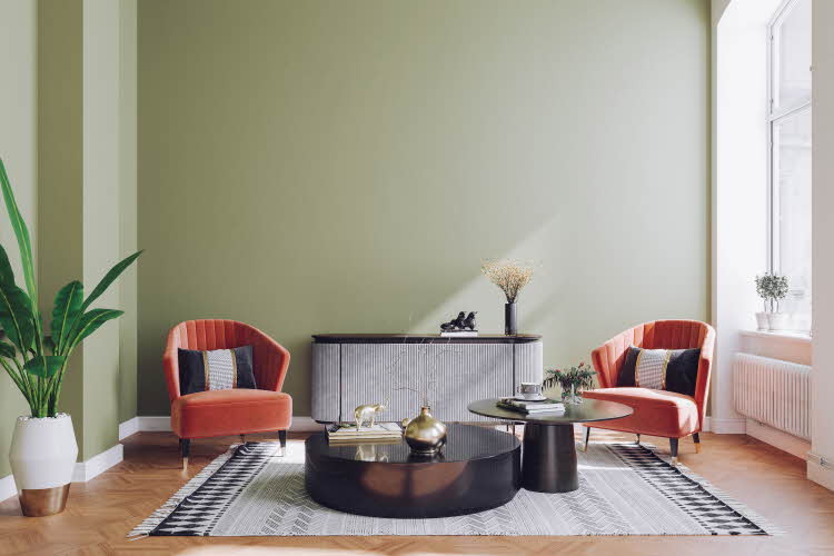 Stue med grønnmalt vegg i pastell, røde stoler, svart marmorbord, plante og gulvteppe.