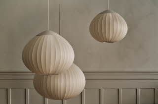 Tre lyse pendellamper med myke former mot en lys vegg.