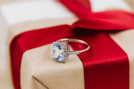 En Jacqueline diamantring som ligger oppe på en innpakket gave.