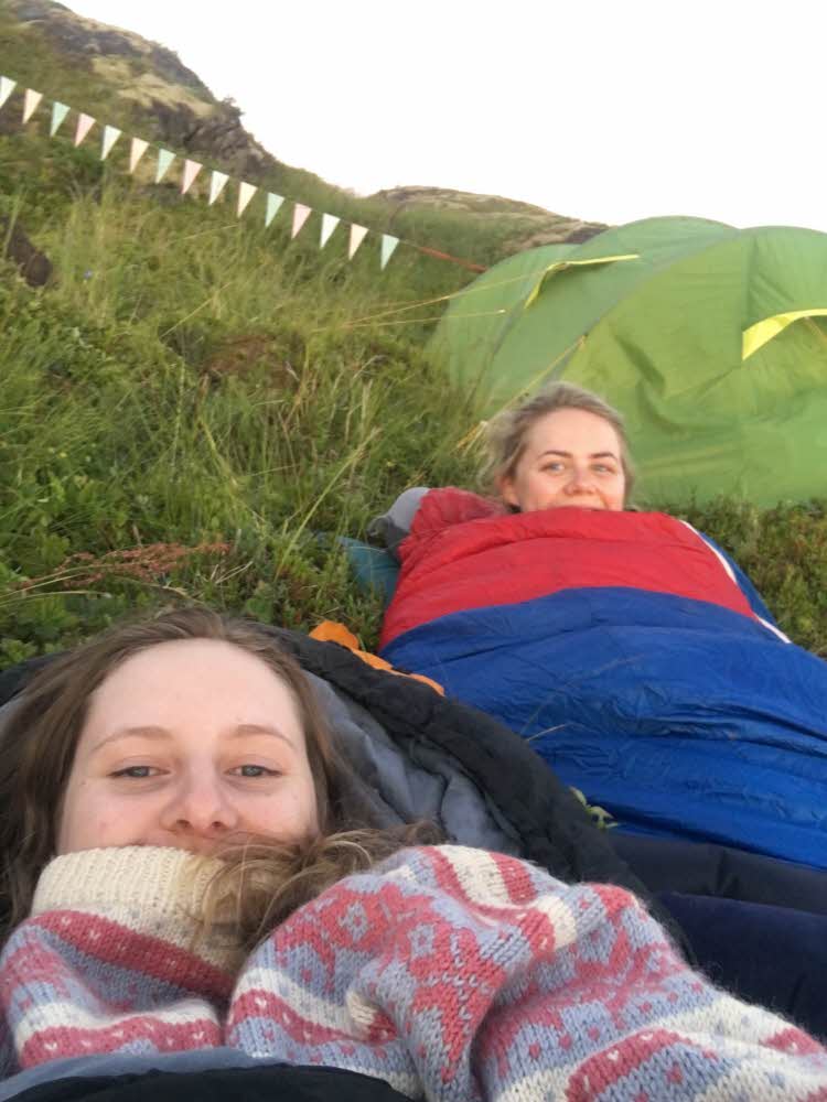 To jenter ligger i sovepose under åpen himmel