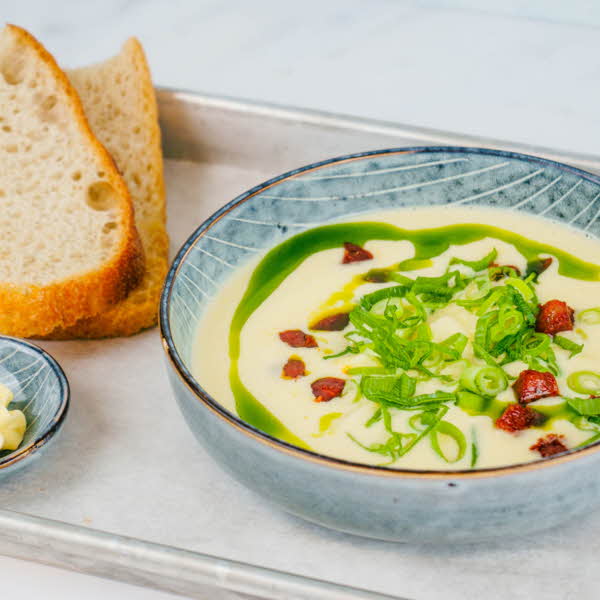 bolle med lys gul suppe, grønt saus og løk med brødskiver ved siden