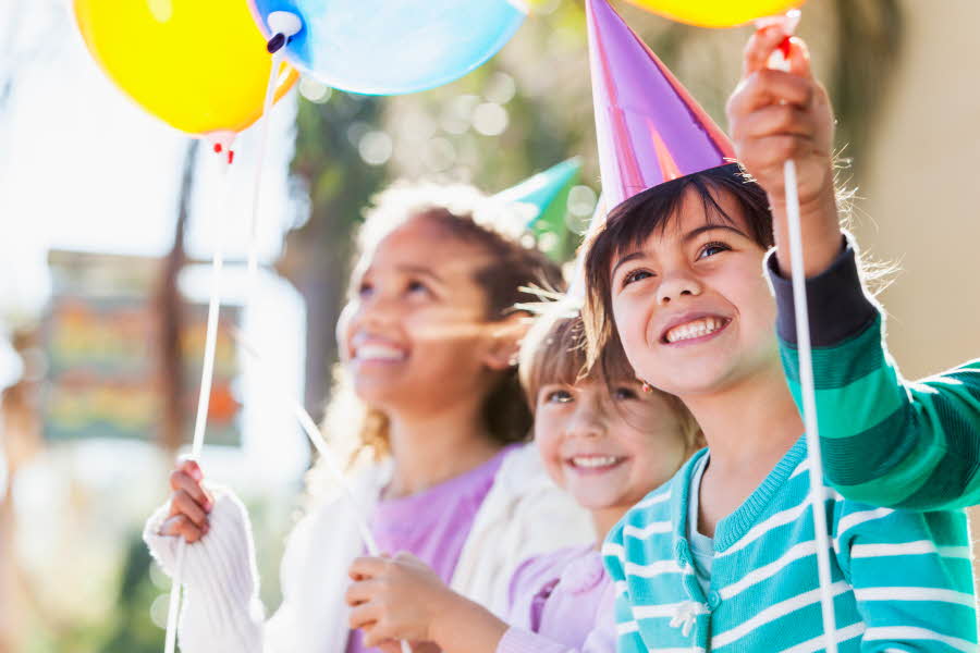 Tre barn som smiler med ballonger i hendene