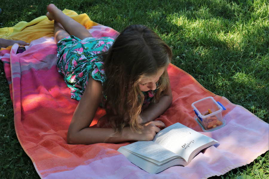 Jente som leser bok ute i hagen