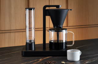 Moderne kaffetrakter med glasskanne og kopp på benk.