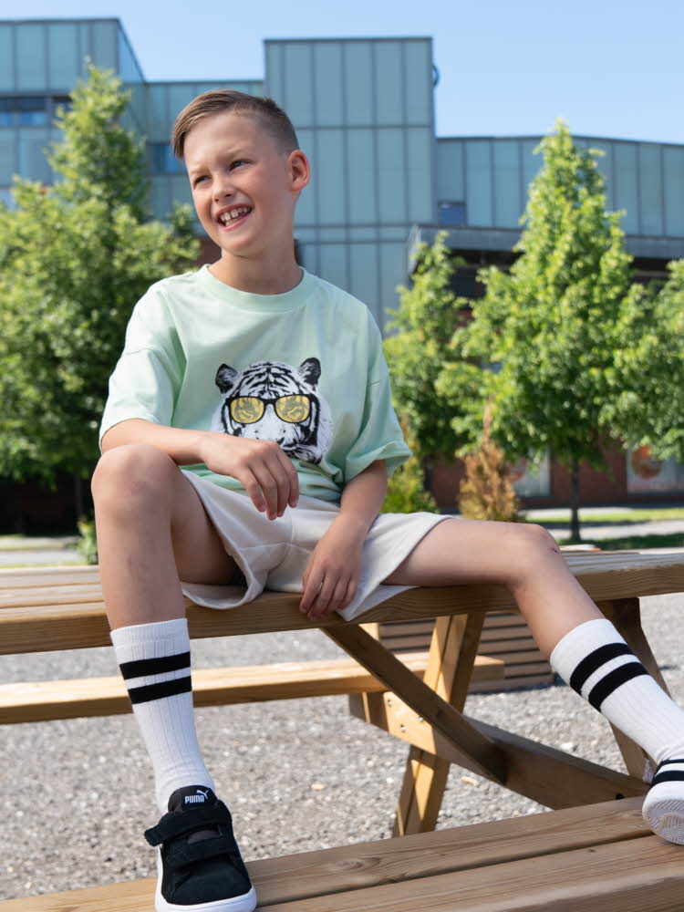 Gutt som sitter på en benk i shorts og t-skjorte