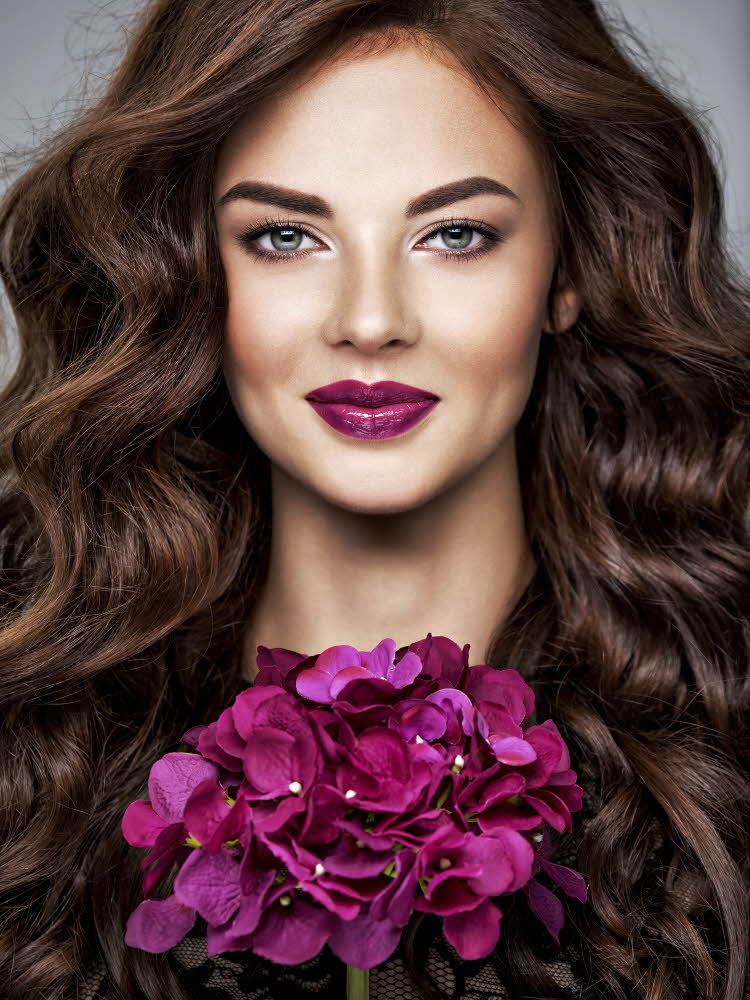 Dame med lilla lepper og holder en lilla blomst til ansiktet