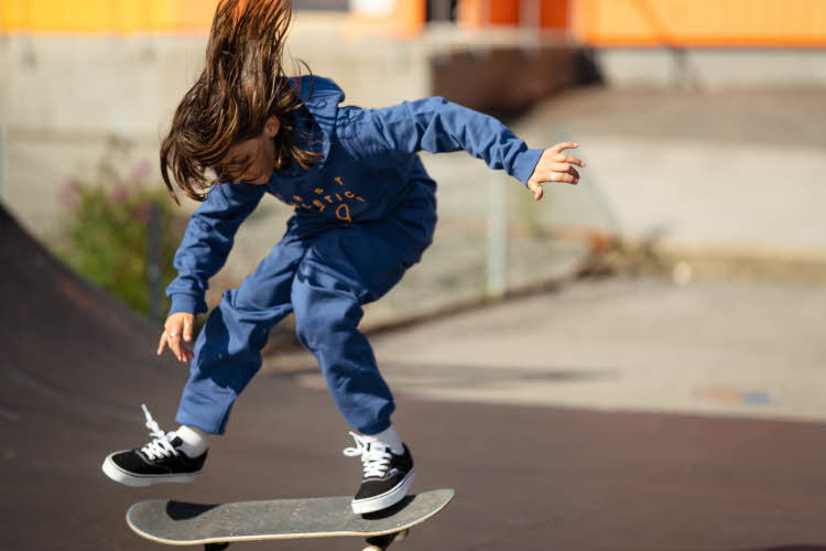 Gutt som trikser på skateboard, ikledd blå joggesett og sorte sko.
