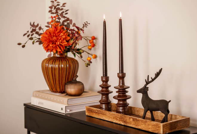 Et sidebord med blomster i vase, noen bøker, et fat med lysestaker og en figur av et reinsdyr