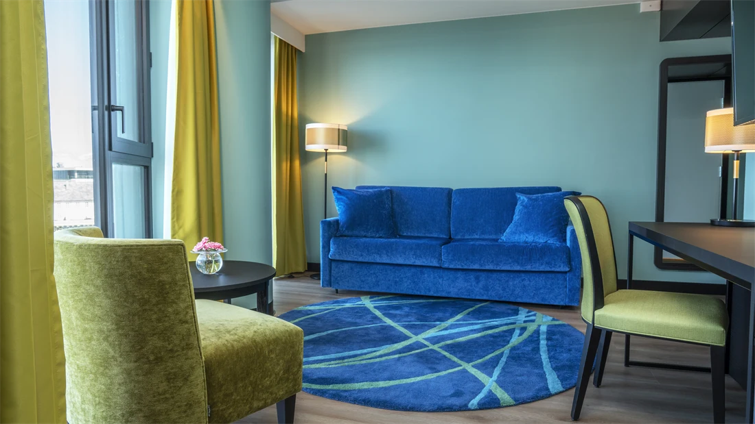 Skrivebord, blå sofa, vindu, gule gardiner, gul lenestol, salongbord, turkis vegg