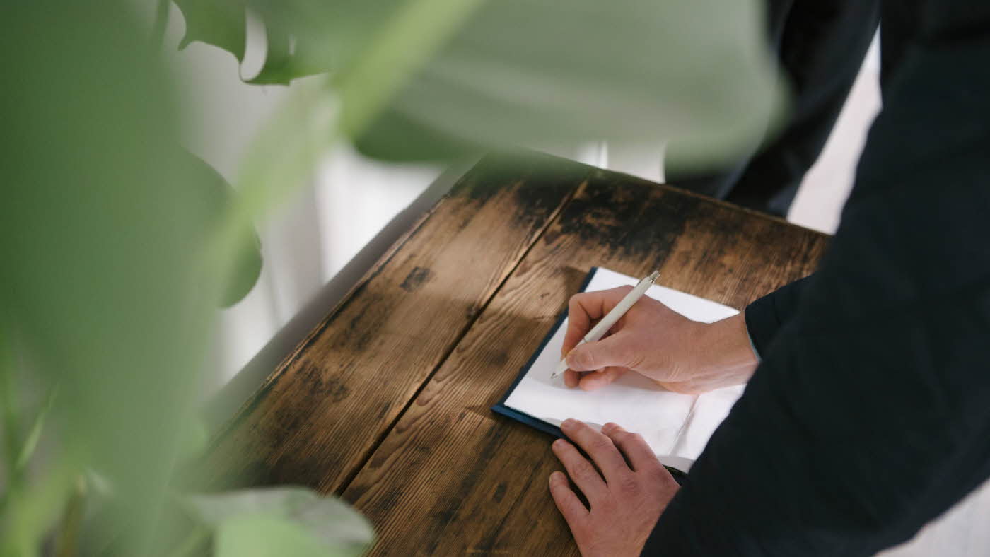 Hånd som signerer ark som ligger på trebord