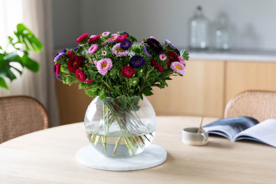rund glass vase med vann og diverse blomstrer i rosa, lilla og rød