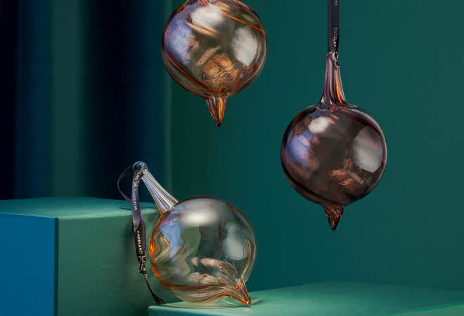 Tre Champagneklang julekuler fra Hadeland Glassverk, to som henger og en som ligger støttet opp.
