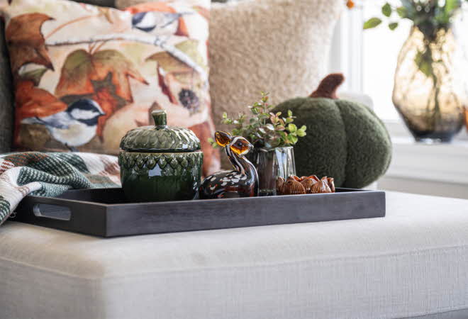 Høstlig interiør med dekor på brett, inkludert keramikk, glassfigur og grønne planter.