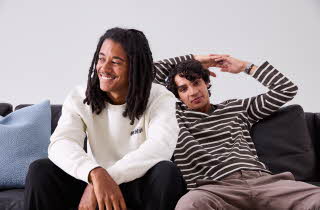 En mann i stripete genser og en mann i hvit genser sitter ved siden av hverandre på en sofa.