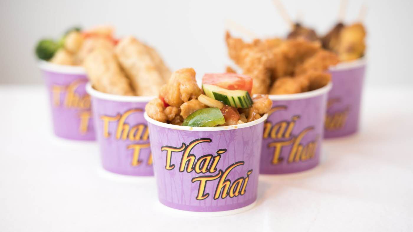 Pappbegere med logo "Thai Thai", inneholder thaimat som vårruller, tempura og wok