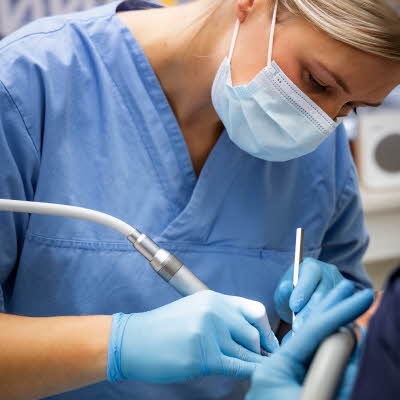 tannlege med munnbind, blå uniform og hansker som jobber med en kunde
