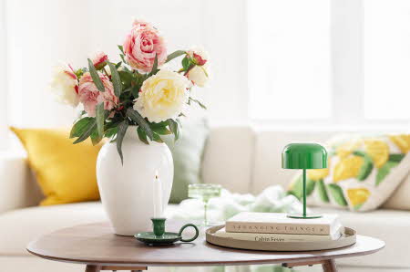 Et stuebord med en vase med blomster, en liten grønn lampe og et par bøker