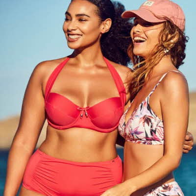 To smilende damer kledd i bikini med sjø og fjell i bakgrunnen