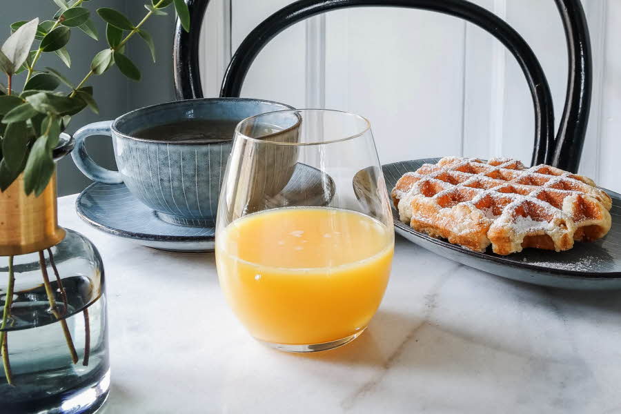 Et glass med appelsinjuice, en kopp med kaffe og en tallerken med vaffel