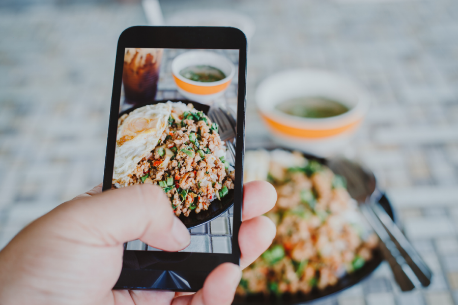 Hånd med mobiltelefon som tar bilde av mat
