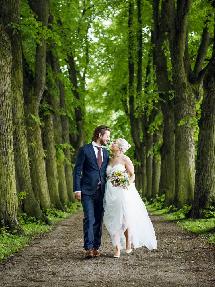 Brudebilde av forelsket nygift par omgitt av trær 