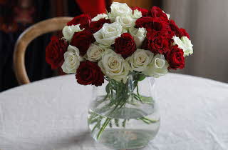 En vase med festroser i rødt og hvitt står på et bord med en hvit duk