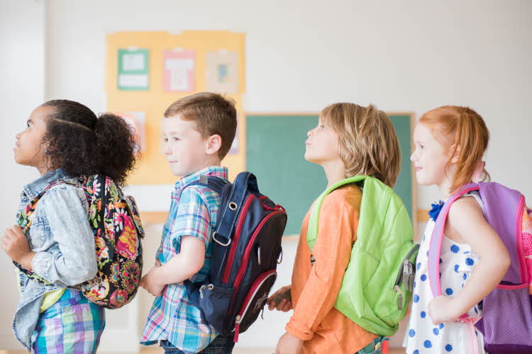 fire barn som står i rekke med ryggsekk på skole