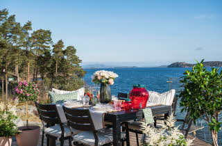 Et bord ute på en terrasse som er dekket til mat og med en vase med blomster i
