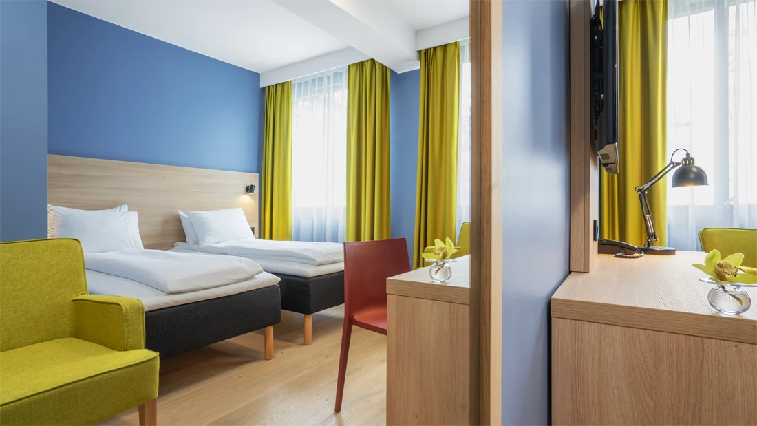 Separate senger, blå vegg, gul stol og gule gardiner på standard rom twin på Thon Hotel Astoria