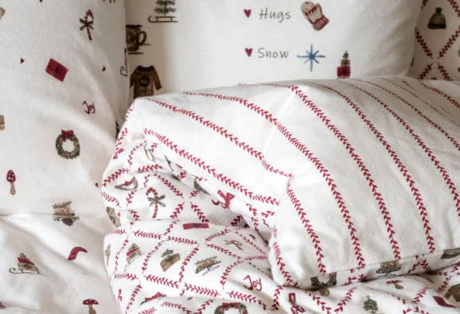 Seng med juleinspirert flanellsengetøy med røde striper og små motiv som kranser og gaver.