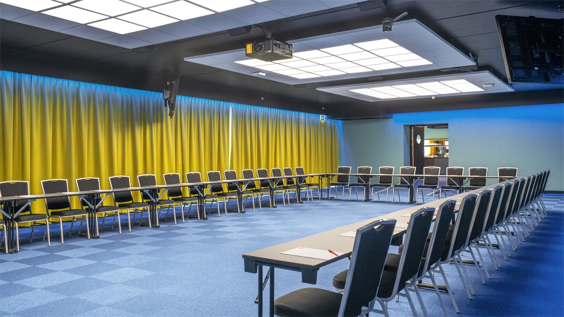 Konferansesal Bjerke satt opp i U-bord med plass til 52 stykker. Blå teppe, gule gardiner og prosjektor på Thon Hotel Linne i Oslo