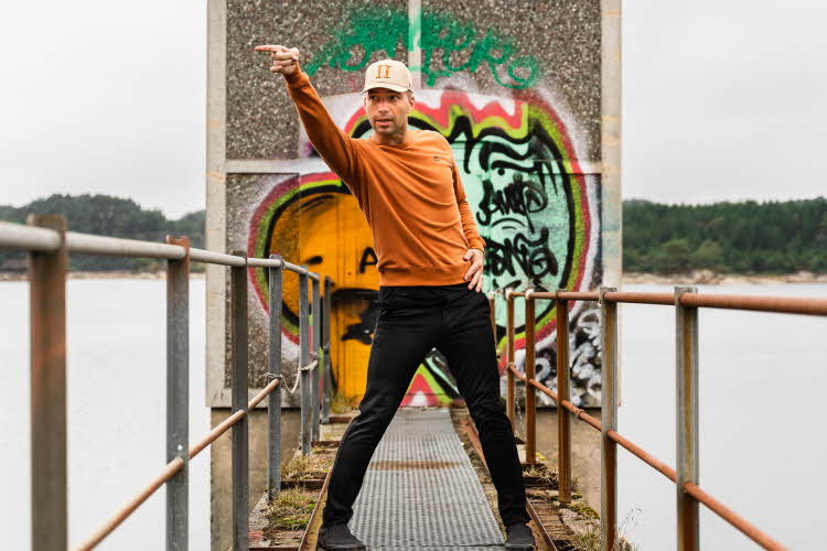 Mann danser som Michael Jackson på en bro med et tårn bak seg. Tårnet er tagget på. Han har på seg oransje genser, sort bukse, sko og beige caps
