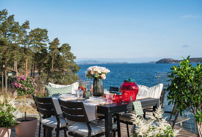 Et bord ute på en terrasse som er dekket til mat og med en vase med blomster i
