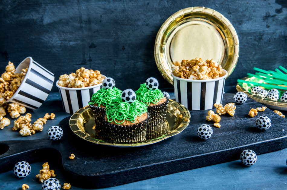 Bord med fotballcupcakes på gulltallerkener og popcorn i skåler 