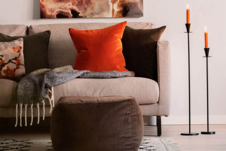 Sofa dekorert med puter, pledd og en lysestake med brennende lys ved siden av