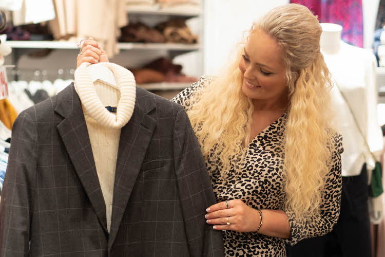 Blond dame holder kleshenger med hvit pologenser og grå blazer