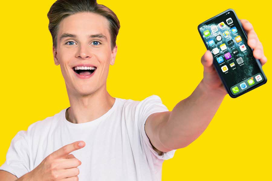 Ung smilende mann i hvit tskjorte som holder en mobiltelefon i hånden