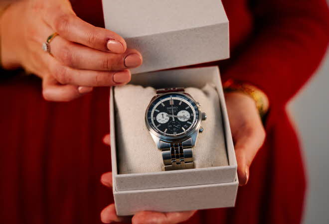 Nærbilde av to hender som holder en boks med en klokke inne i.