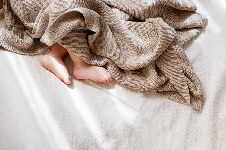 Baby som ligger i senga og sover meg brun strikket teppe over seg