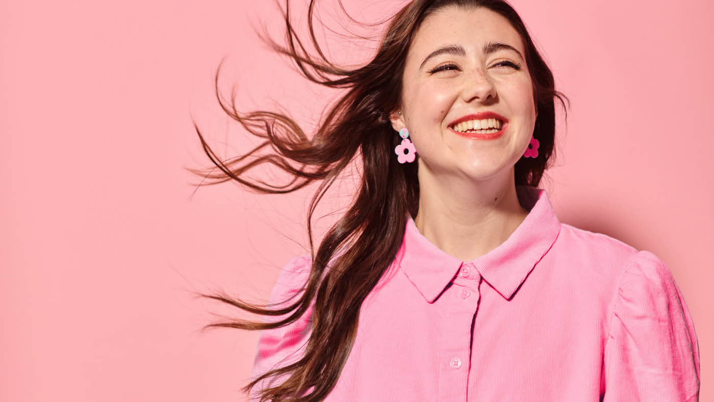 Dame som smiler med rosa skjorte, øredobber og bakgrunn