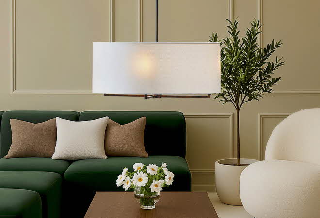 En stor, rund taklampe henger over et stuebord med en grønn sofa bak