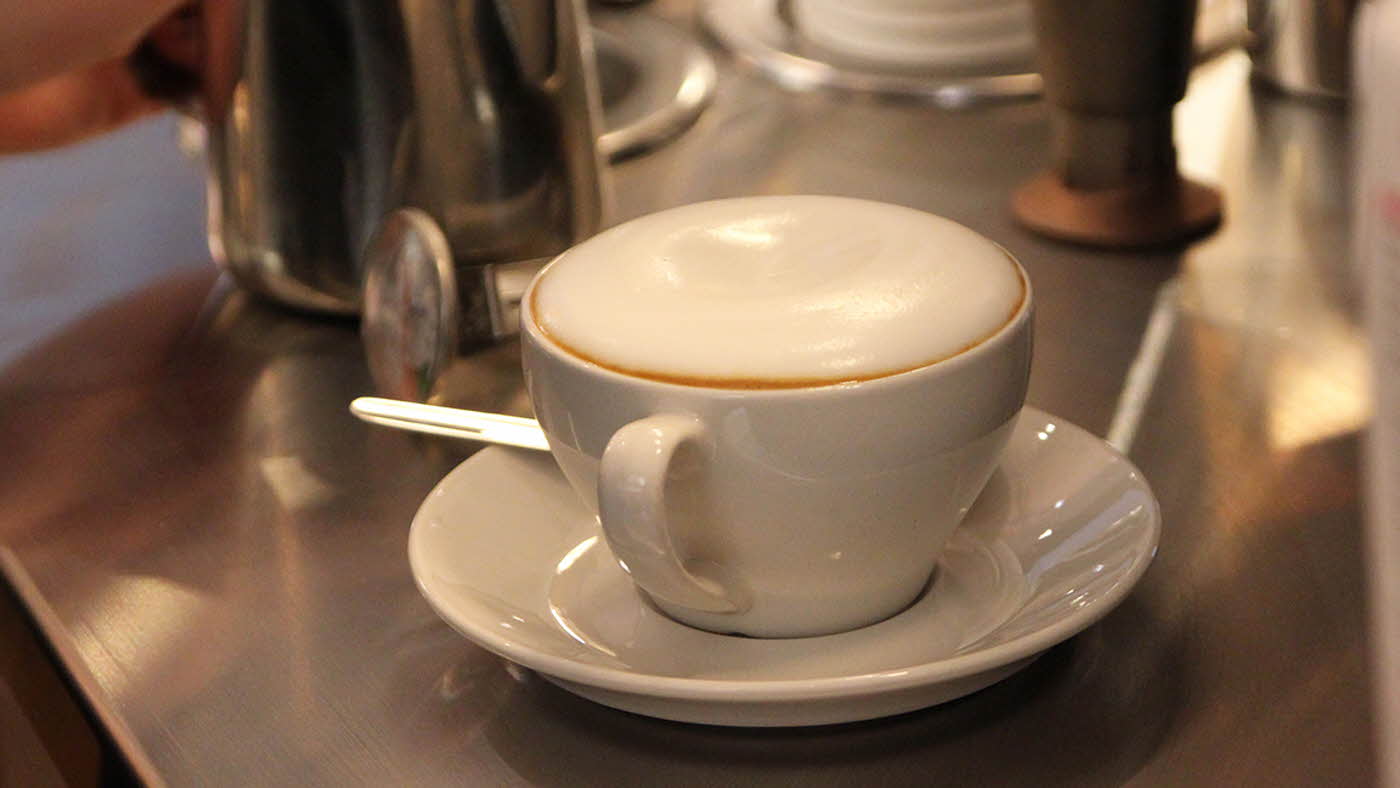 Bord med bakst, juice og kaffe  Kaffe med mønster i kremmen  Kopp med kaffe og krem 