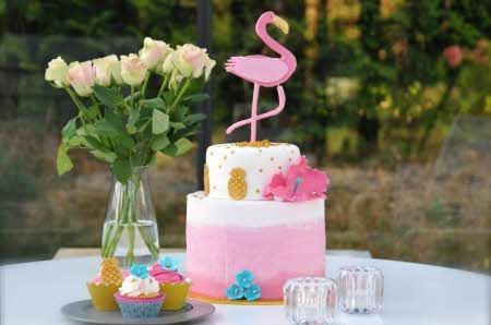 En kake på et bord med lys, muffins og blomster ved siden av