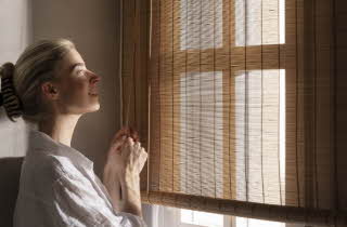 En kvinne som holder i tråden til en solskjermer og smiler ut av vinduet