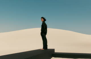 En kvinne som står på en sanddyne ikledd sorte klær