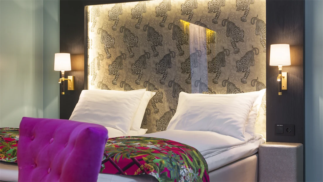 Dobbeltseng med mønstrede sengeteppe og lilla stol på buisness room på Thon hotel Terminus i Oslo sentrum nær Jernbanetorget