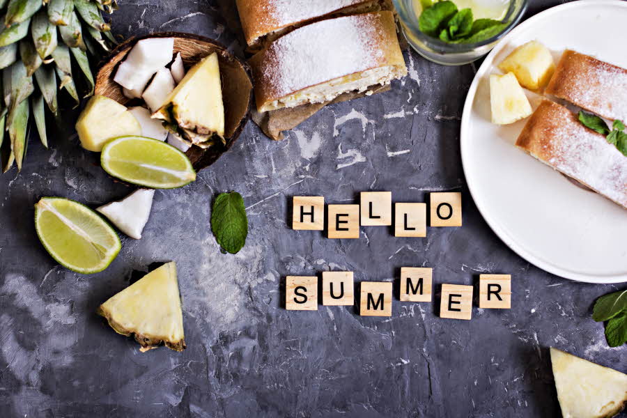 Flat lay av lime og ananas og scrabble-brikker hvor det står «hello summer»
