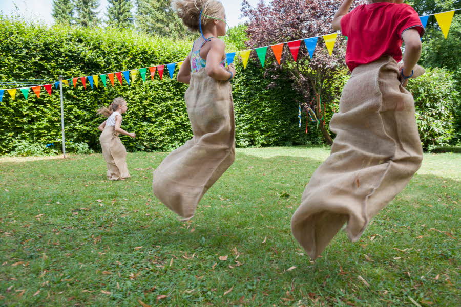 Barn leker sekkeløp i en hage dekorert med fargerike vimpler