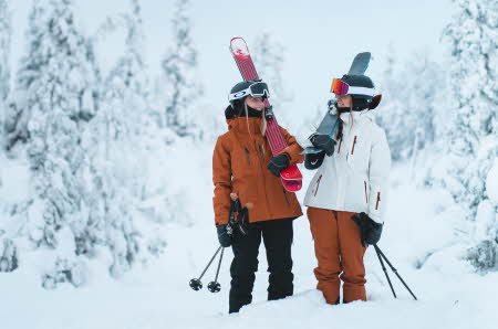 To kvinner holder alpinski og er kledd i vinterjakke og skibukse